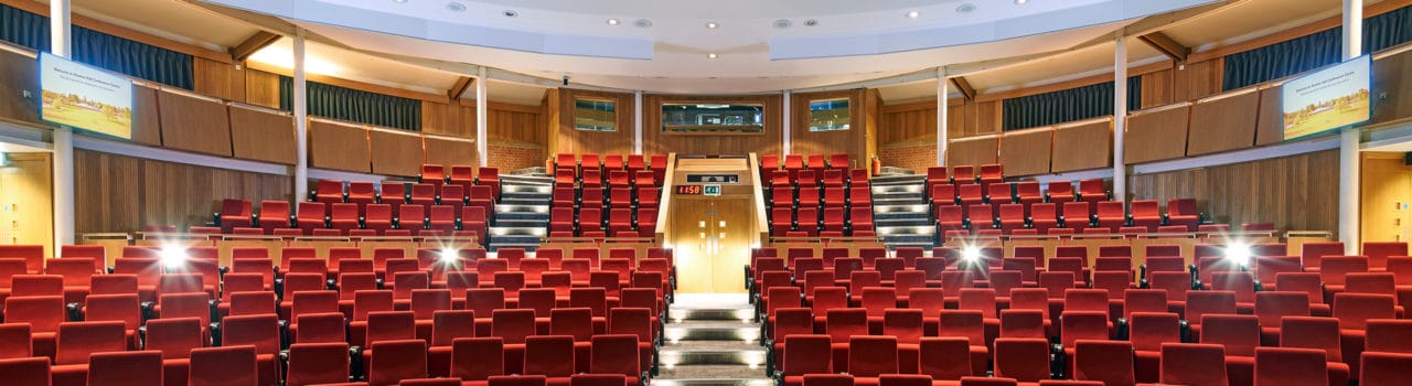 Francis Crick Auditorium, looking towards the technicians booth. Bright read matt seats, and lights gleaming.