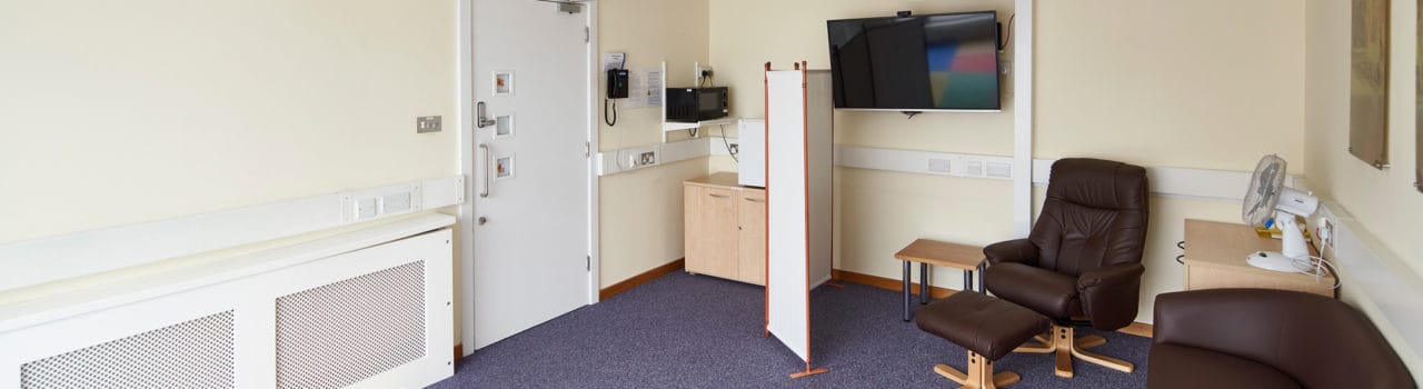 The Family Room at Hinxton Hall Conference Centre, showing comfortable seating, a padded play area, microwave, fridge, highchair, and a screen