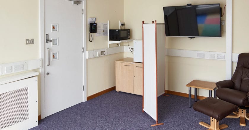 The Family Room at Hinxton Hall Conference Centre, showing comfortable seating, a padded play area, microwave, fridge, highchair, and a screen