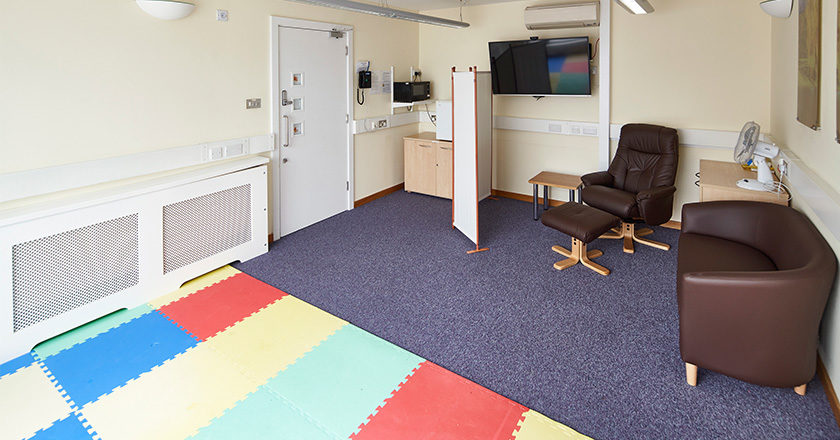 The Family Room at Hinxton Hall Conference Centre, showing comfortable seating, a padded play area, microwave, fridge, highchair, and a screen