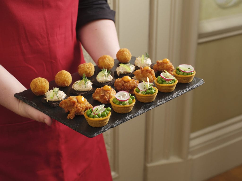 Waitress with a red apron holding plate of canapés