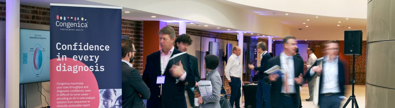 An exhibitor stand (Congenica) and representative talking to delegate