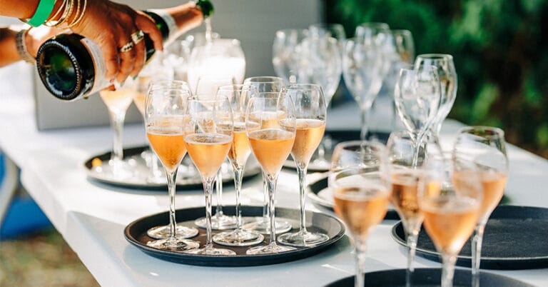 Glasses of sparkling ros&eacute; wine being poured on a tray.