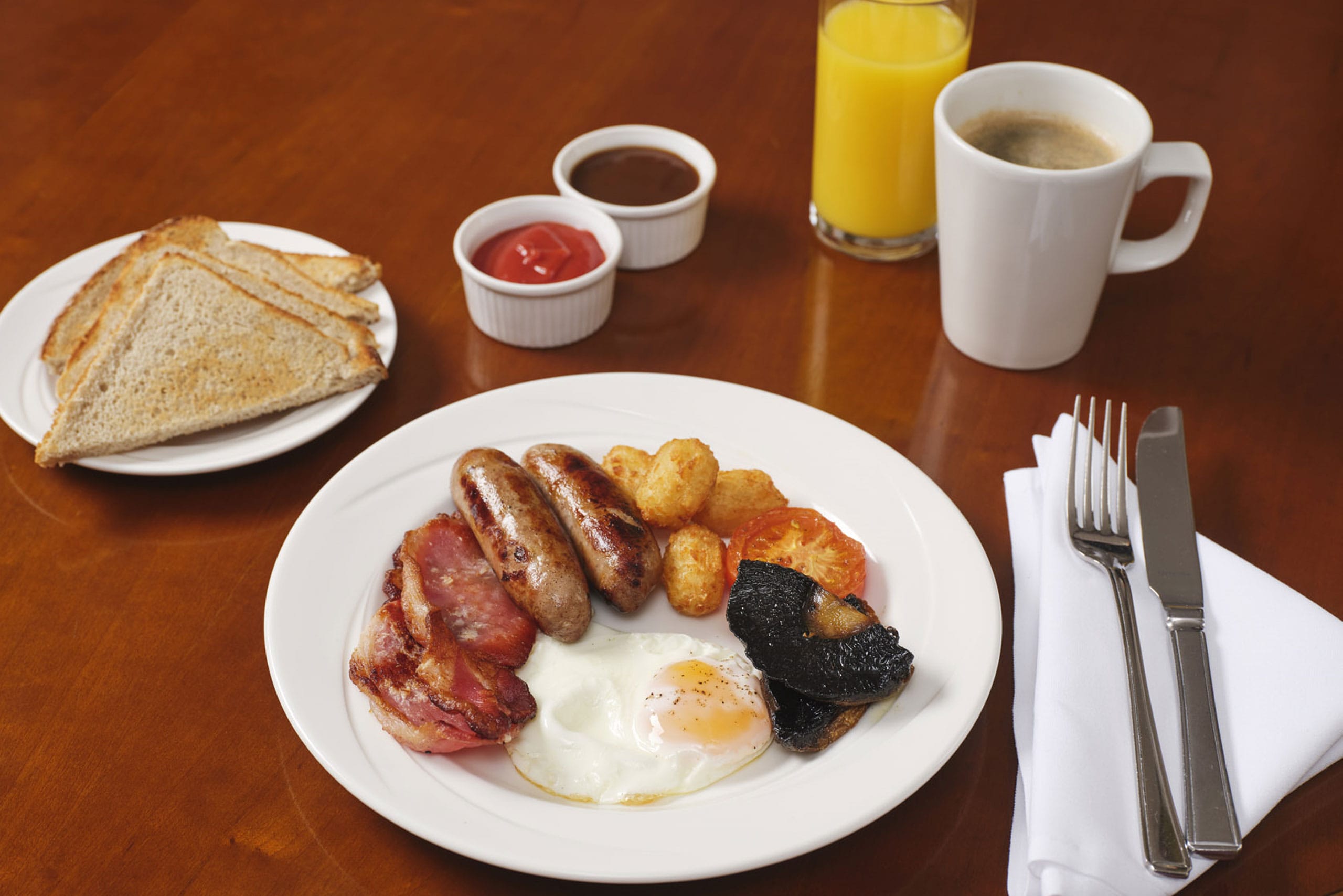 A photo of breakfast at Hinxton Hall Hotel, showing a full english breakfast, toast, orange juice and coffee.