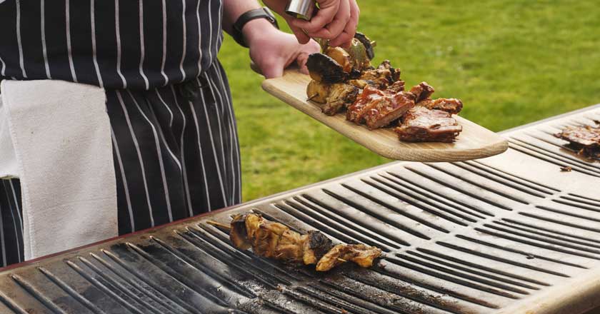 A barbecue at Hinxton Hall. A chef is taking some meat off the grill and placing it on a wooden board.