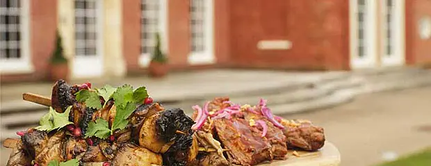 BBQ meat on a wooden board, held in front of Hinxton Hall.