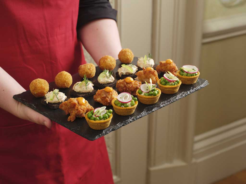 A server in a red apron holding a board of wedding canapes.
